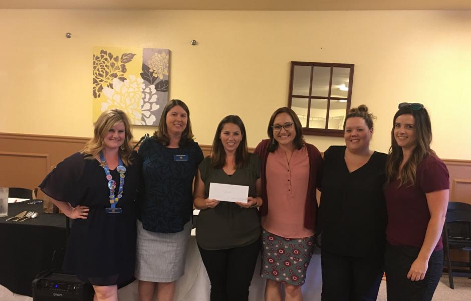 6 women standing, smiling, holding a donation check