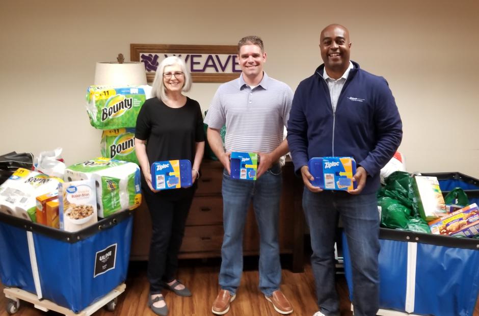 3 people with 2 bins on new items for donation, paper towels,  tupperware, dish towels, cereal.