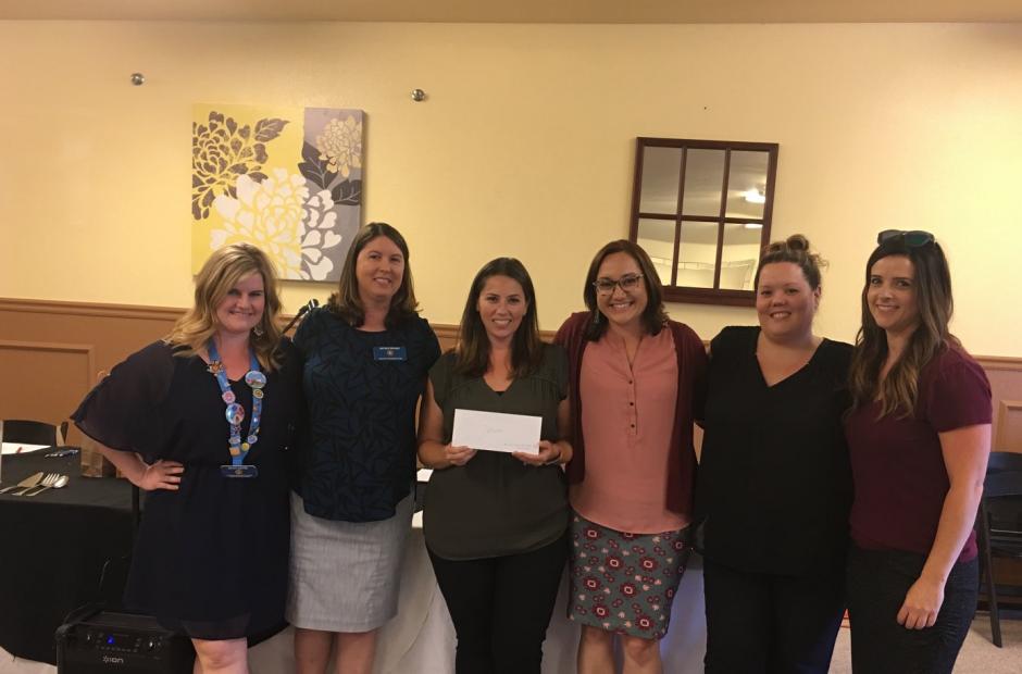 6 women standing, smiling, holding a donation check